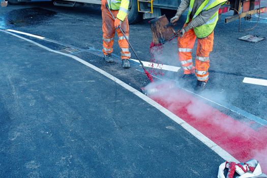 Road workers applying hot red road marking paint on new build road
