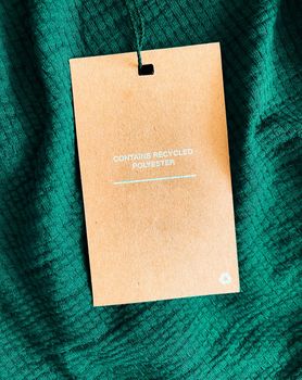 Contains recycled polyester fashion label tag, sale price card on luxury emerald green fabric background, shopping and retail