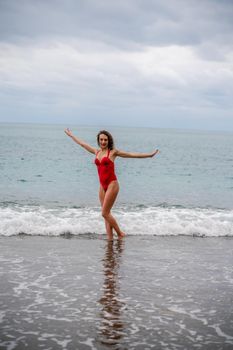 A beautiful and sexy brunette in a red swimsuit on a pebble beach, Running along the shore in the foam of the waves