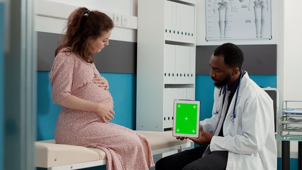 Obstetrician holding greenscreen on digital tablet at checkup visit