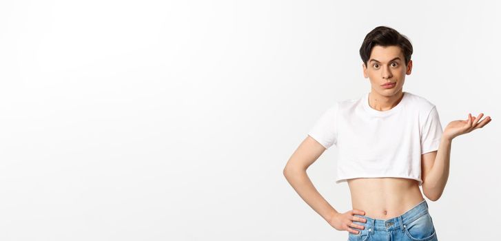 Handsome androgynous man in crop top looking confused, shrugging clueless, standing over white background