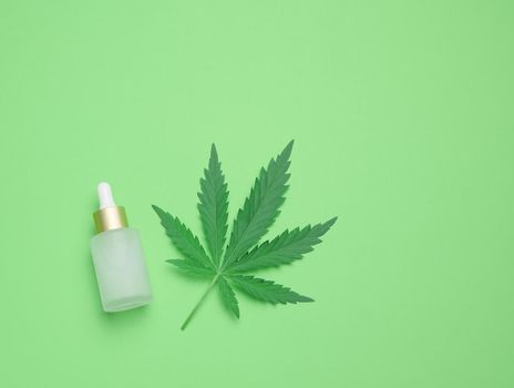 White glass bottle with pipette and green cannabis leaf on a green background