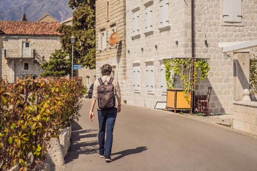Man tourist enjoying Colorful street in Old town of Perast on a sunny day, Montenegro. Travel to Montenegro concept. Scenic panorama view of the historic town of Perast at famous Bay of Kotor on a beautiful sunny day with blue sky and clouds in summer, Montenegro, southern Europe