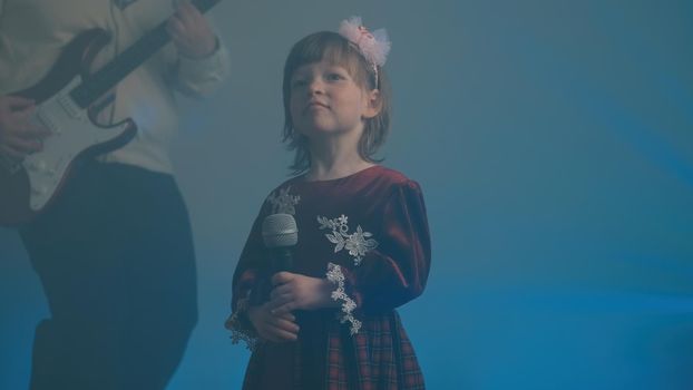 Little girl in vintage dress sings on stage, her father plays an electric guitar