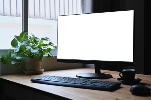 Simple workplace with computer pc, coffee cup and potted plant on wooden table.