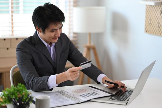 Asian businessman holding debit card and making banking online on laptop computer.