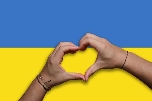 Hand making a heart sign over Ukrainian flag. Concept of ending the war and pray for Ukraine.