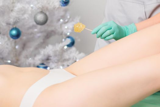 Young woman getting wax epilation of legs