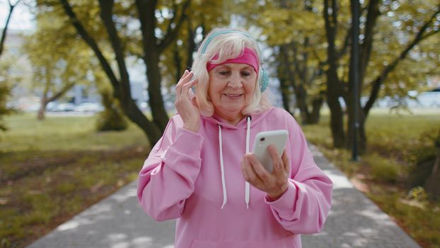 Athletic senior sport runner woman wearing earphones listening music from smartphone in morning park
