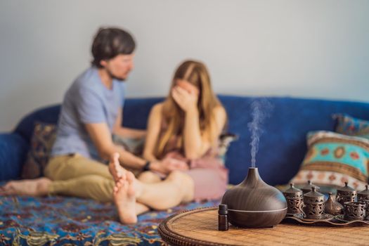 Man comforting his upset partner at home in living room. Aromatherapy Concept. Wooden Electric Ultrasonic Essential Oil Aroma Diffuser and Humidifier. Ultrasonic aroma diffuser for home. Woman resting at home