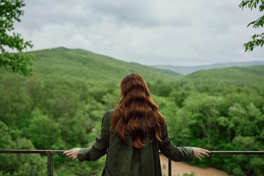 a red-haired woman with beautiful, well-groomed, long hair stands with her back to the camera and enjoys the view of the forest