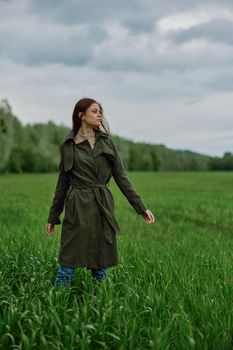 a woman in a long raincoat stands in tall green grass in a field in rainy weather in spring