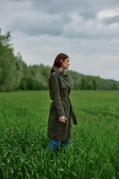a woman in a long raincoat stands in tall green grass in a field in rainy weather in spring