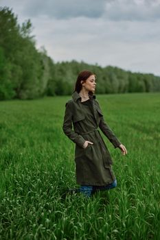 a beautiful woman in a dark coat stands in a green field in the spring in rainy weather