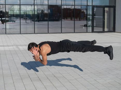 A man in black sportswear jumps while doing push-ups outdoors.