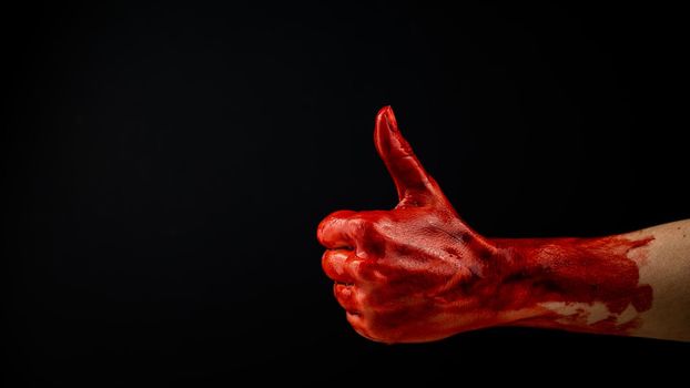 A woman's hand stained with blood shows a thumbs up on a black background.