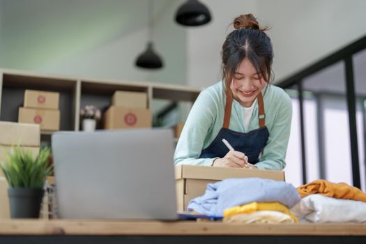 A portrait of a small startup, and SME owner, an Asian female entrepreneur, is writing down information on a notepad to organize the product before packing it into the inner box for the customer