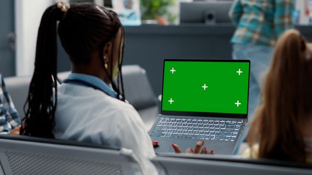 General practitioner holding laptop with greenscreen in waiting room