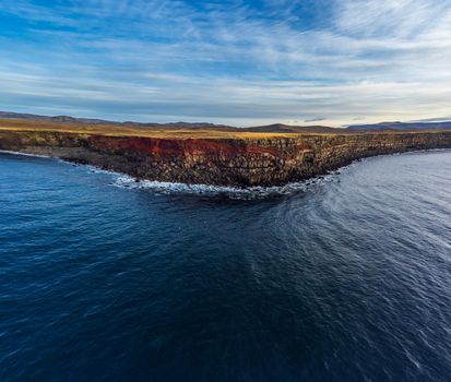 Steep cliffs with red seams in Iceland, view from the oceans