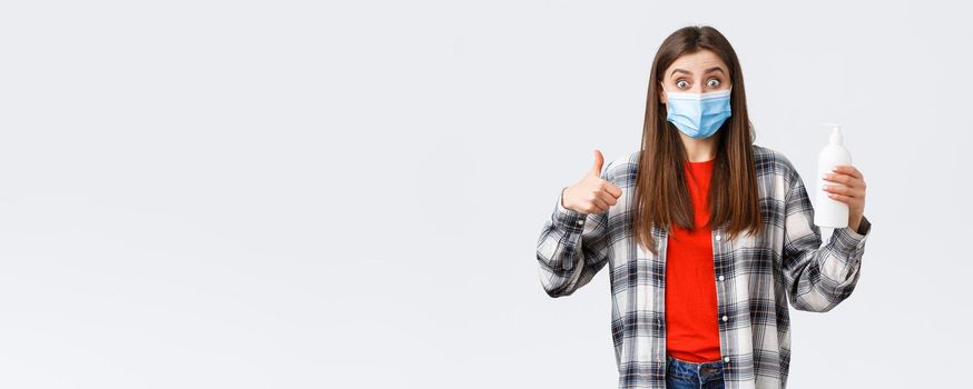 Coronavirus outbreak, leisure on quarantine, social distancing and emotions concept. Excited and satisfied girl in medical mask promote great hand sanitizer, preventing virus soap, thumb-up