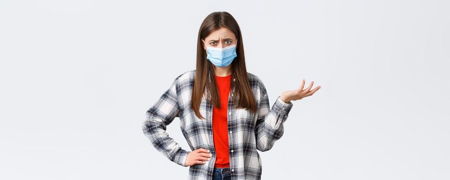 Coronavirus outbreak, leisure on quarantine, social distancing and emotions concept. Confused and bothered young woman cant understand this, shrug and stare puzzled camera, medical mask