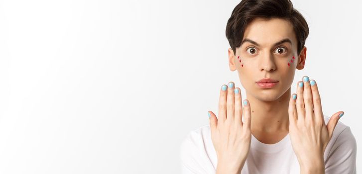 People, lgbtq and beauty concept. Beautiful gay man showing blue nail polish on fingernails and looking at camera, have manicure, standing over white background