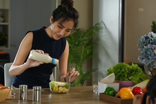 Cheerful healthy woman pouring sauce on salad in a glass bowl. Diet and Healthy food concept.