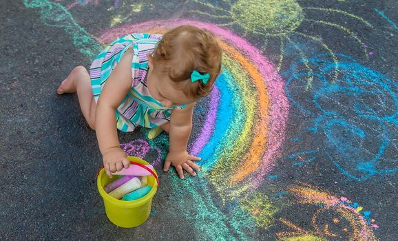 Baby draws a rainbow on the pavement with chalk. Selective focus.