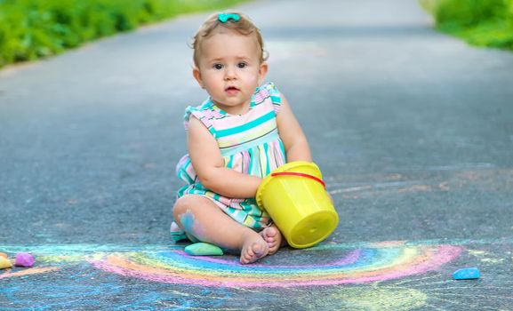 Baby draws a rainbow on the pavement with chalk. Selective focus.