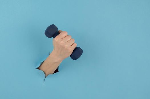 A female hand sticking out of a hole from a blue background holds a dumbbell.