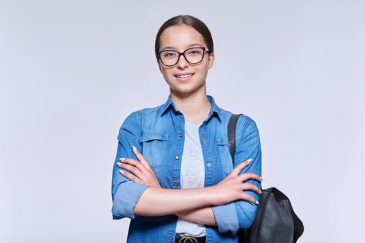 Teenage student girl in glasses with backpack looking at camera, on light background