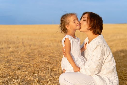 Mom kisses daughter cheek wheat field. Mother kiss little girl