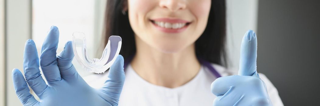 Stomatologist holding mouthguard for teeth and showing thumb up sign
