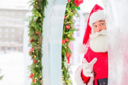 Santa claus peeks out of Christmas decorations outdoors