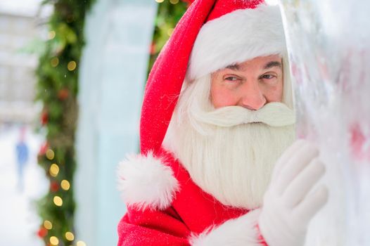 Santa claus peeks out of Christmas decorations outdoors