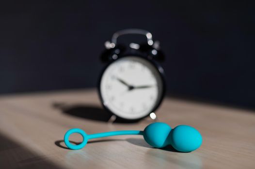 Alarm clock and vibrator on the table. Time for training intimate muscles. Vaginal balls strengthen the pelvic floor muscles for powerful orgasms.