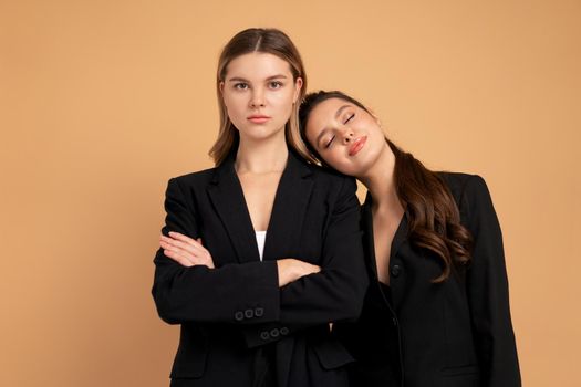 Two young business woman dressed black suit standing studio orange color background