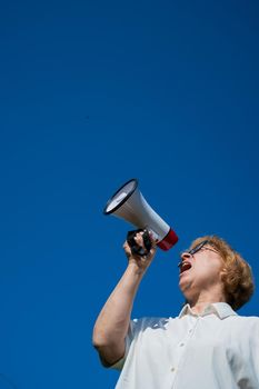 An emotional elderly woman pushes demands into a megaphone. An angry retired woman is fighting for the rights of older people. The female leader of the rally voiced claims to the loudspeaker.