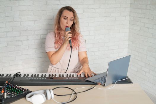 A woman records a vocal lesson using a laptop and accompanying on a keyboard while at home. The teacher sings a song into the microphone and plays the electronic piano. A blogger is recording a video.