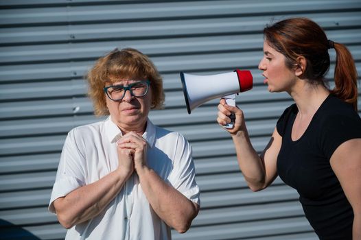 The conflict of generations. An angry middle-aged woman yells at an elderly mother through a megaphone. An adult daughter screams at an unhappy pensioner over a loudspeaker. Quarrel in the family.