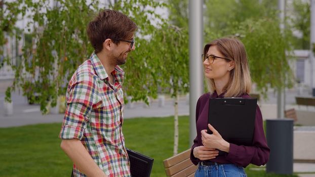 Two college students meeting and talking on campus, in a park.