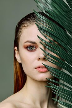 a close beauty portrait of a beautiful woman standing holding a tropical palm leaf in her hand, bringing it to her face, looking into the camera. Vertical photo without retouching of problem skin