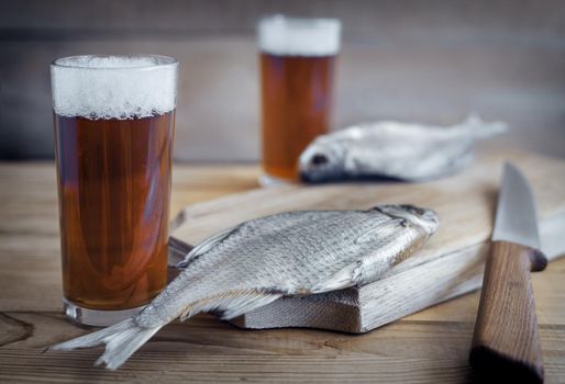 On a wooden table two glasses of beer, next to the cutting Board dried fish and a knife.