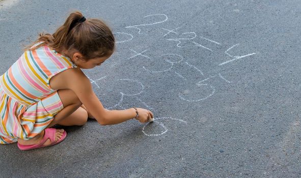 The child is doing chalk lessons on the asphalt. Selective focus.