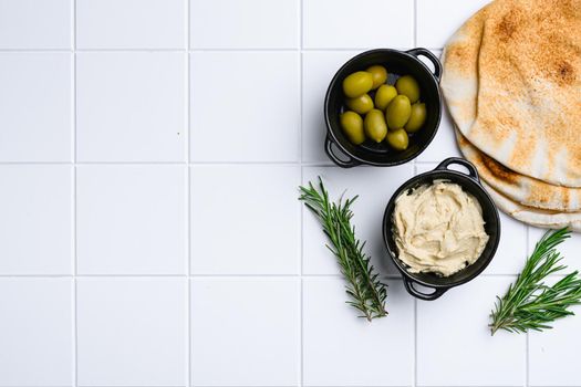 Hummus and pita bread set, on white ceramic squared tile table background, top view flat lay, with copy space for text