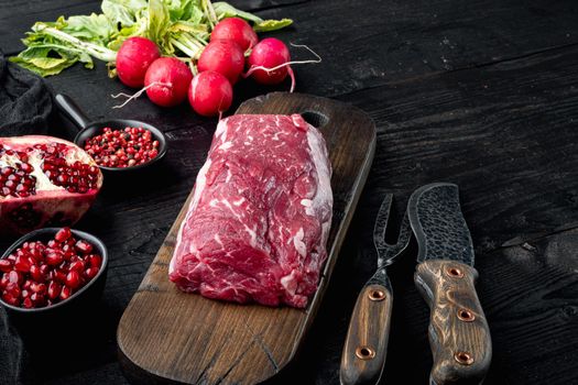 Fresh and raw beef meat. Whole piece of tenderloin with steaks and spices ready to cook, on black wooden table background, with copy space for text