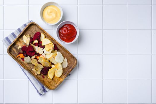 Dried vegetables chips, on white ceramic squared tile table background, top view flat lay, with copy space for text