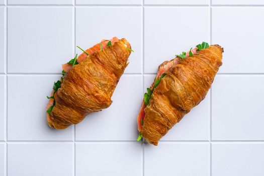 Croissant sandwich with salmon, on white ceramic squared tile table background, top view flat lay