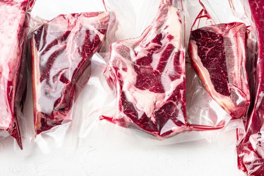 Raw beef meat in the vacuumed skin pack, tomahawk, t bone, club steak, rib eye and tenderloin cuts, on white stone background