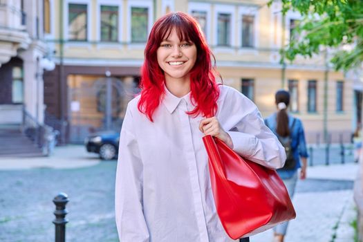 Teenage fashionable smiling female with red dyed hair looking at camera